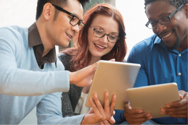Three people wearing glasses smiling and looking at two tablets